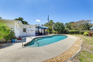 Une piscine dotée d’un patio couvert, entourée d’un jardin bien entretenu et d’un bâtiment blanc.