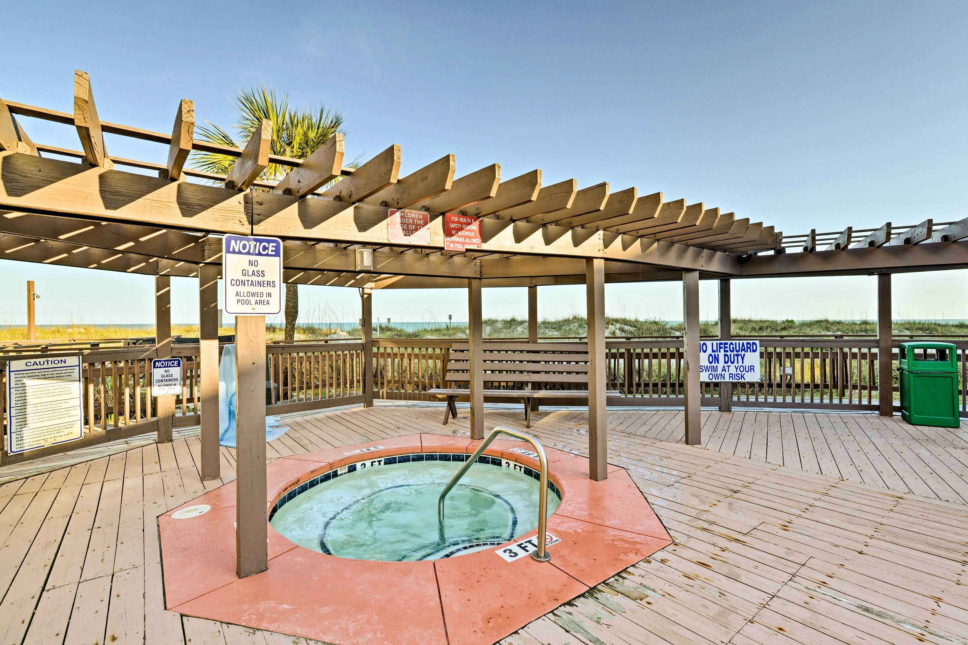 Een houten terras met een jacuzzi, een houten pergola en picknicktafels.