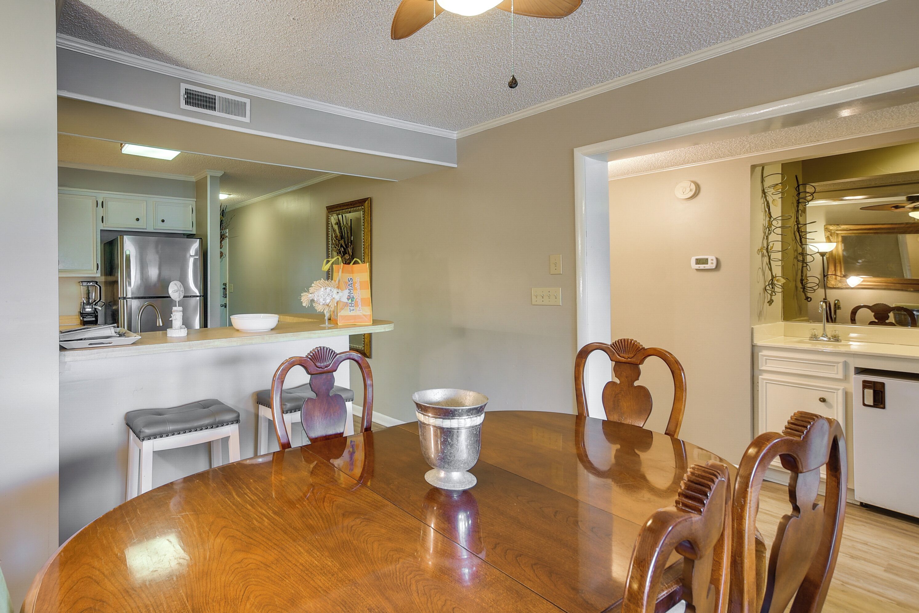 Un coin repas avec une table et des chaises en bois, une cuisine à l’arrière-plan et un ventilateur de plafond.