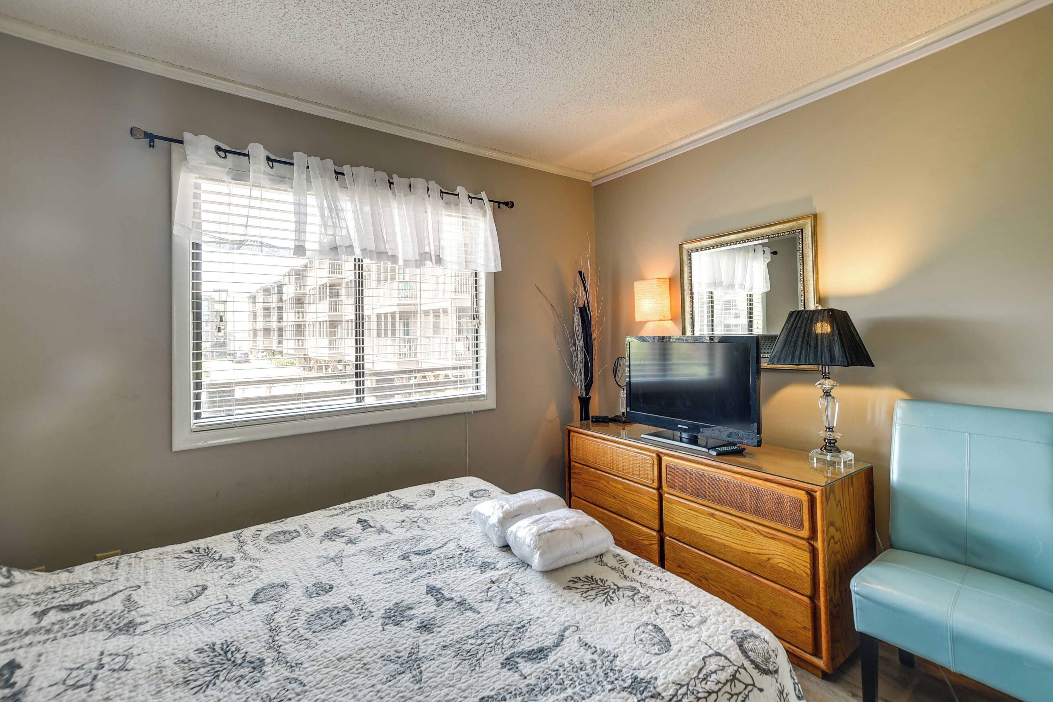 A bedroom with a bed, dresser, TV, lamp, and a blue chair.
