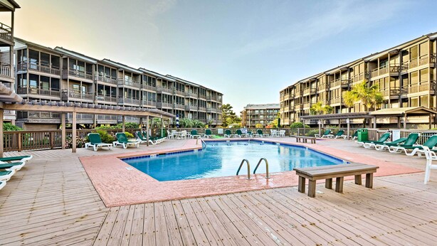 A pool area with a wooden deck, lounge chairs, and a swimming pool. - Walk to Coast: North Myrtle Beach Condo w/ Pool! (North Myrtle Beach)