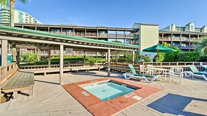 A pool area with a wooden deck, lounge chairs, and a covered seating area. - Walk to Coast: North Myrtle Beach Condo w/ Pool! (North Myrtle Beach)