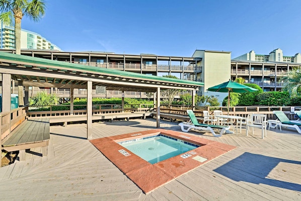 A pool area with a wooden deck, lounge chairs, and a covered seating area. - Walk to Coast: North Myrtle Beach Condo w/ Pool! (North Myrtle Beach)