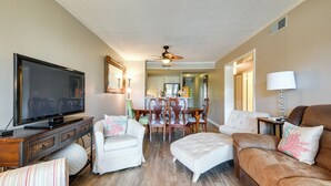 A living room with a television, white sofas, a brown leather sofa, a dining area with a table and chairs, and a ceiling fan. - Walk to Coast: North Myrtle Beach Condo w/ Pool! (North Myrtle Beach)