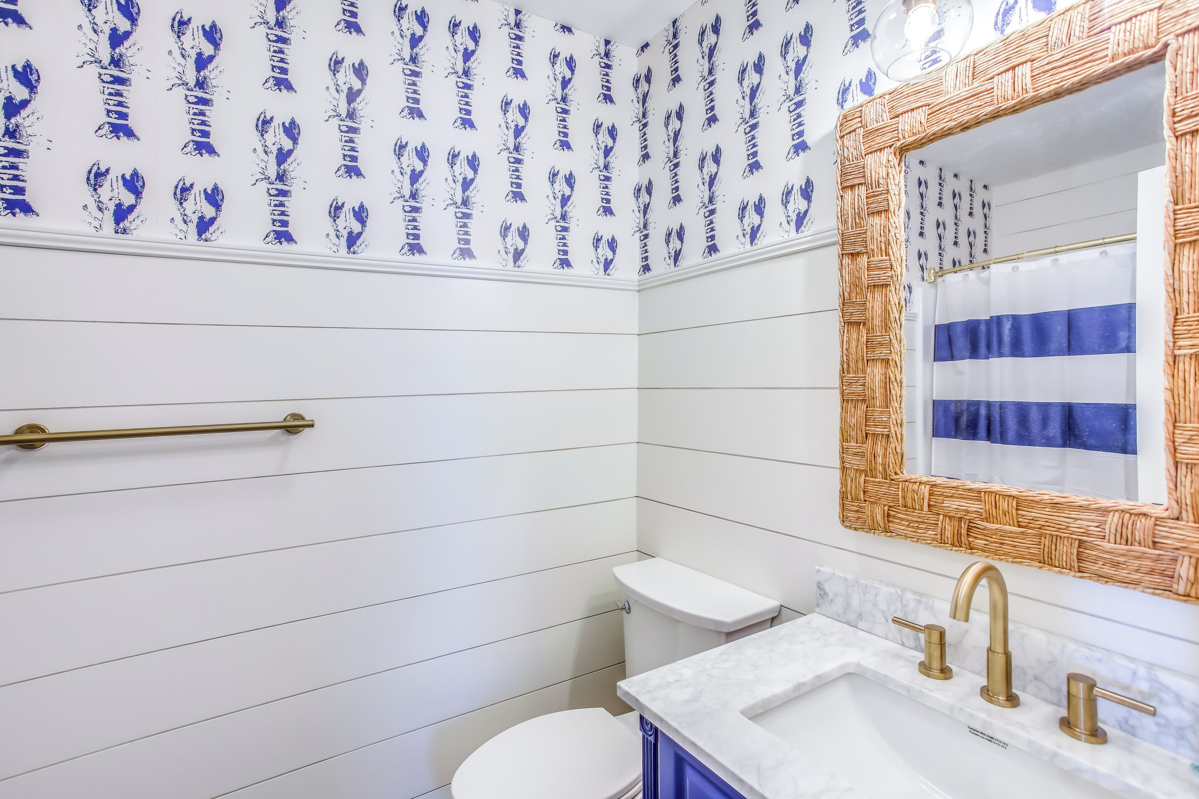 Une salle de bain avec des murs carrelés de carreaux blancs, des toilettes blanches, un lavabo avec des robinets dorés et un miroir avec un cadre tressé.