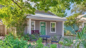 Una piccola casa con una porta verde, un portico con due sedie e un tavolino.