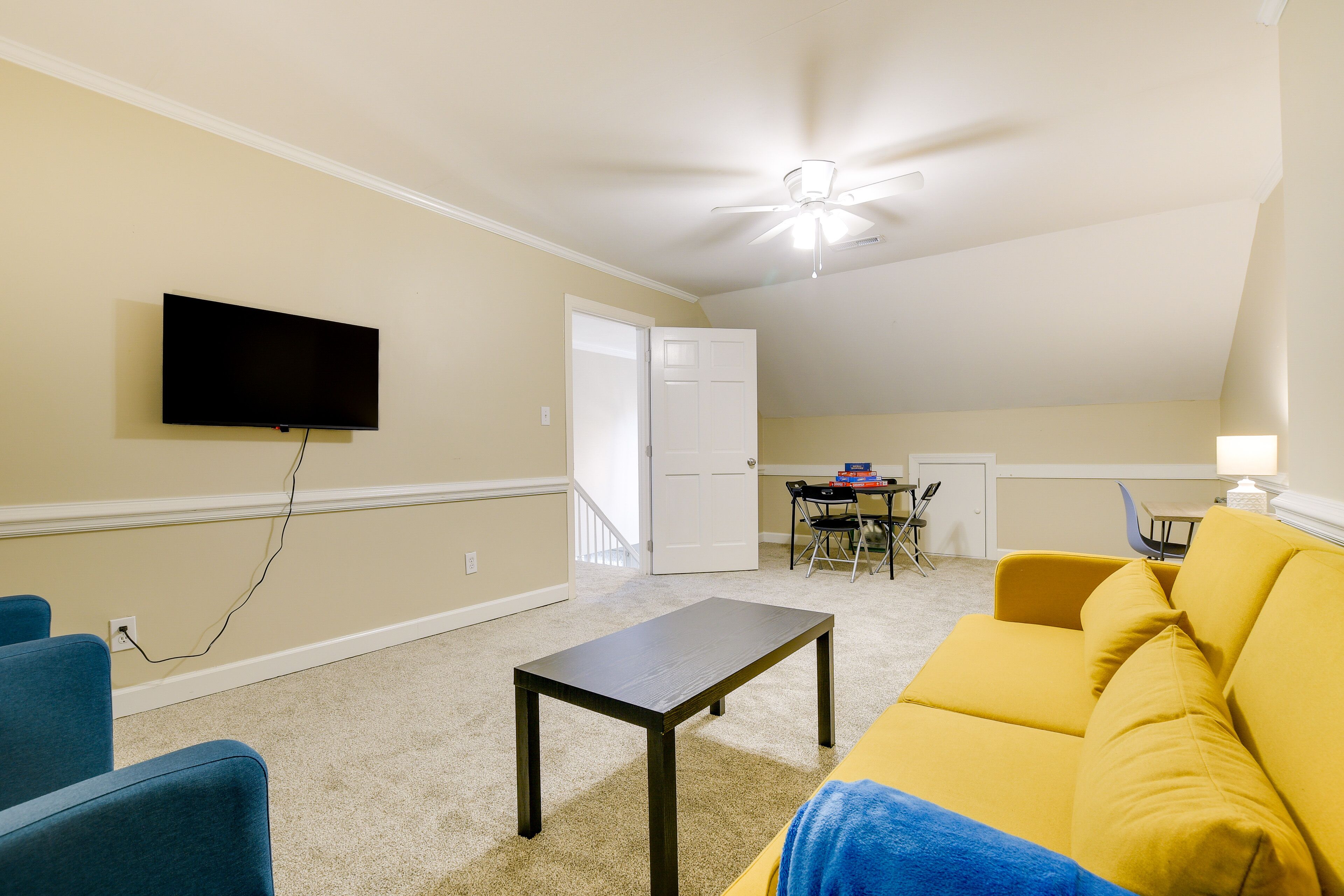 A living room with a flat-screen TV, a dark wooden coffee table, a yellow sofa, and blue chairs.
