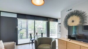 Ett modernt vardagsrum med en soffa, en rund fåtölj, en tv-apparat på ett träskåp och ett stort fönster med persienner.