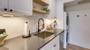 Ett modernt kök med vita skåp, en diskho i rostfritt stål och en inbyggd tvättmaskin.