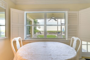 A dining area with a round table, white chairs, and a large window with shutters. - Longboat Key Vacation Rental: Direct Beach Access! (Longboat Key)