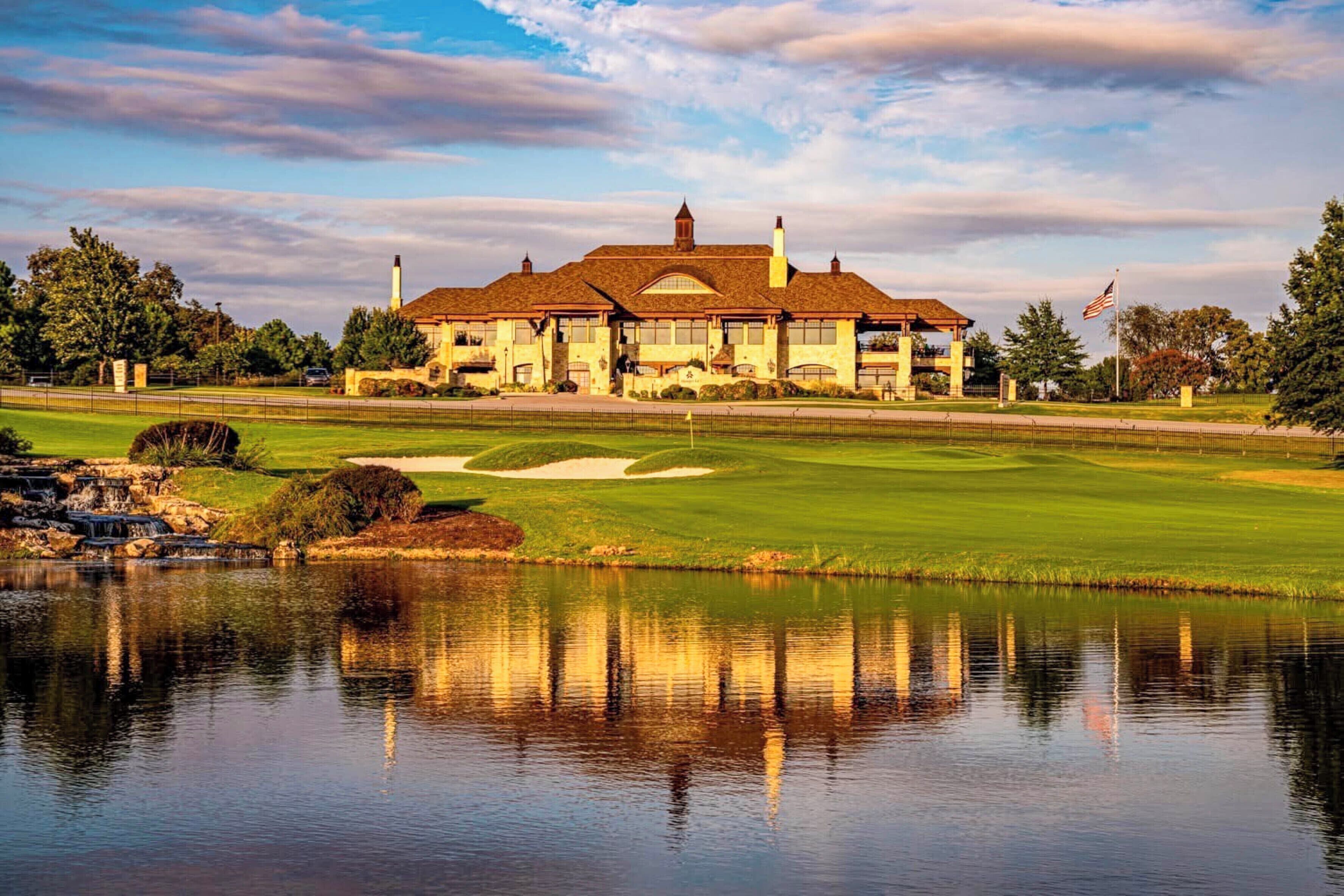 A large building with a prominent tower, surrounded by a well-maintained golf course and a body of water reflecting the structure.