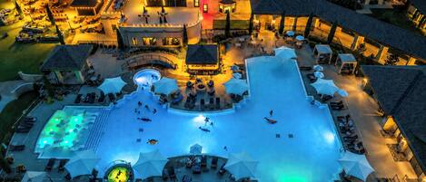 An aerial view of a hotel with a central swimming pool, outdoor seating areas, and multiple buildings.