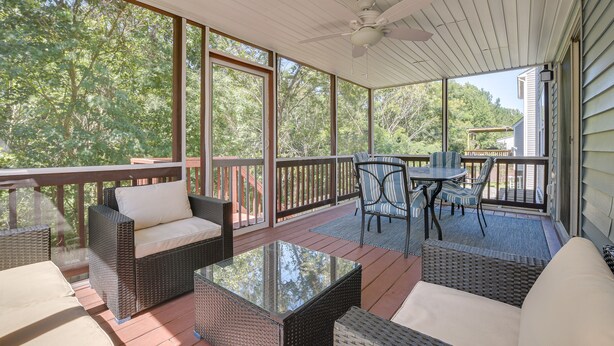 A covered outdoor deck with wicker furniture, a glass table, and a view of the surrounding trees. - Raleigh Home w/ Modern Adjustable Sleeping System (Raleigh)