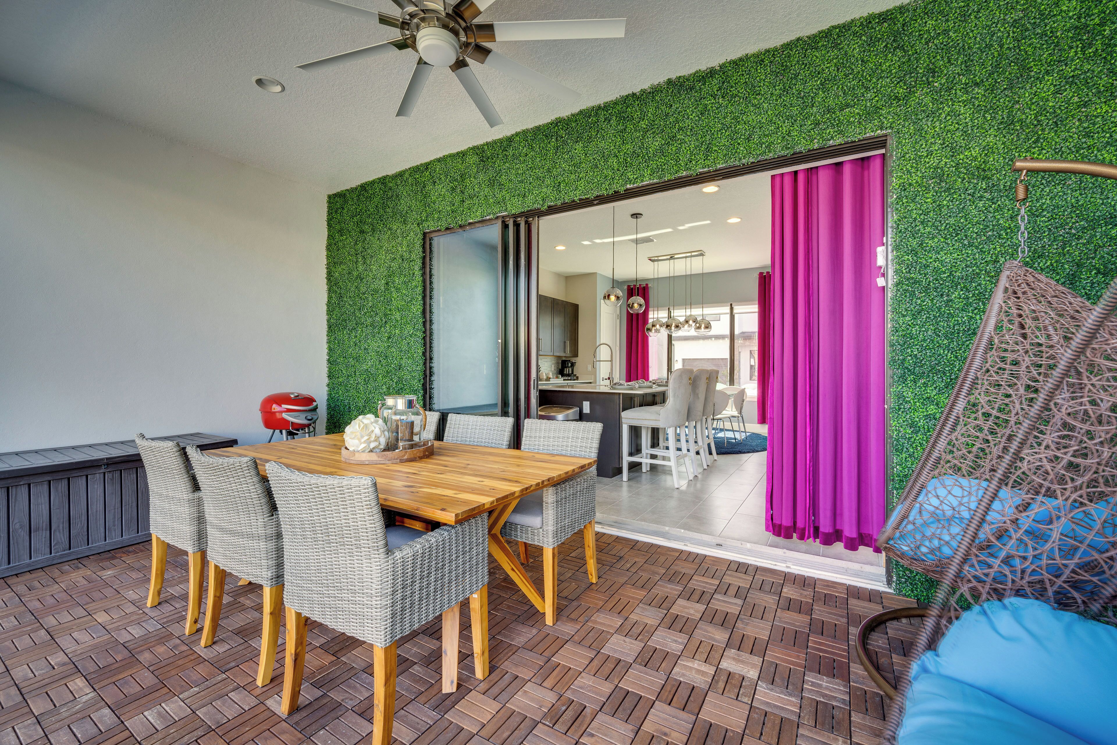 An outdoor dining area with a wooden table and wicker chairs, a ceiling fan, and a green wall.