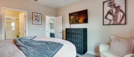 Une chambre à coucher avec un lit, une commode, une chaise, un ventilateur de plafond et un tableau accroché au mur.