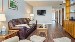 A living room with a brown leather sofa, a glass coffee table, and a television mounted on the wall. - Walk to Restaurants: Downtown Leesburg Townhome! (Leesburg)