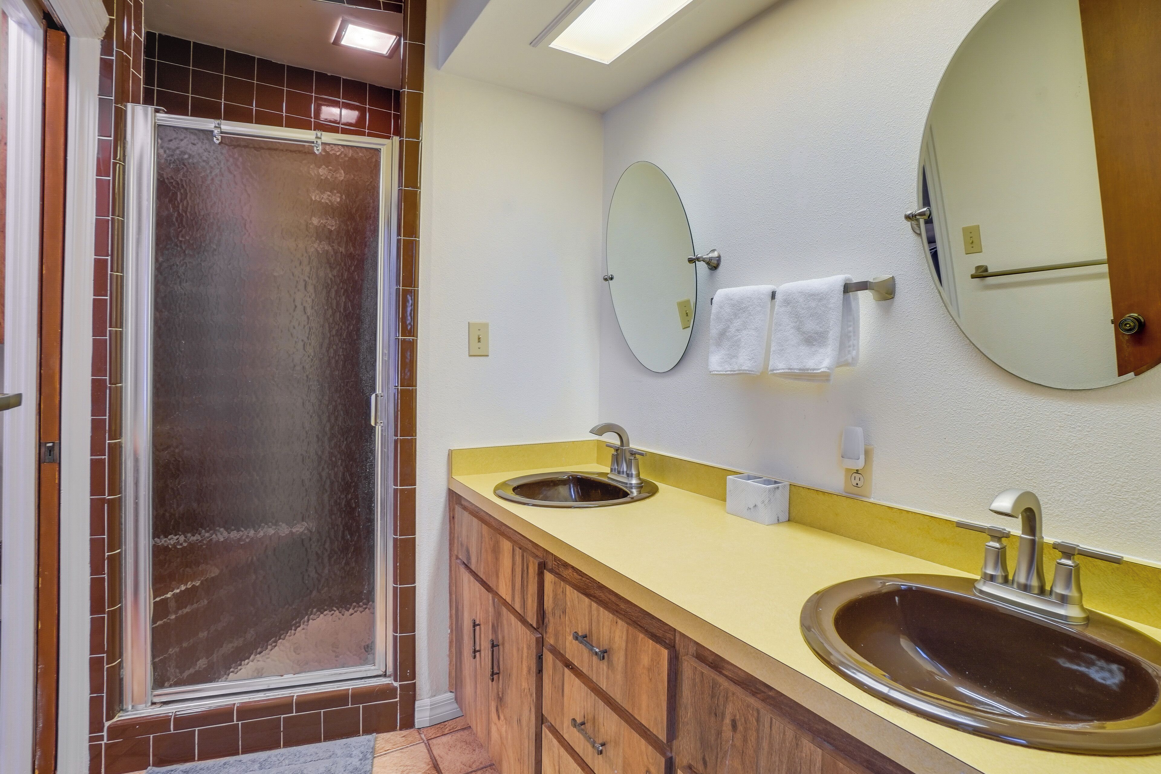 A bathroom with a shower, two sinks, wooden cabinets, and two mirrors.