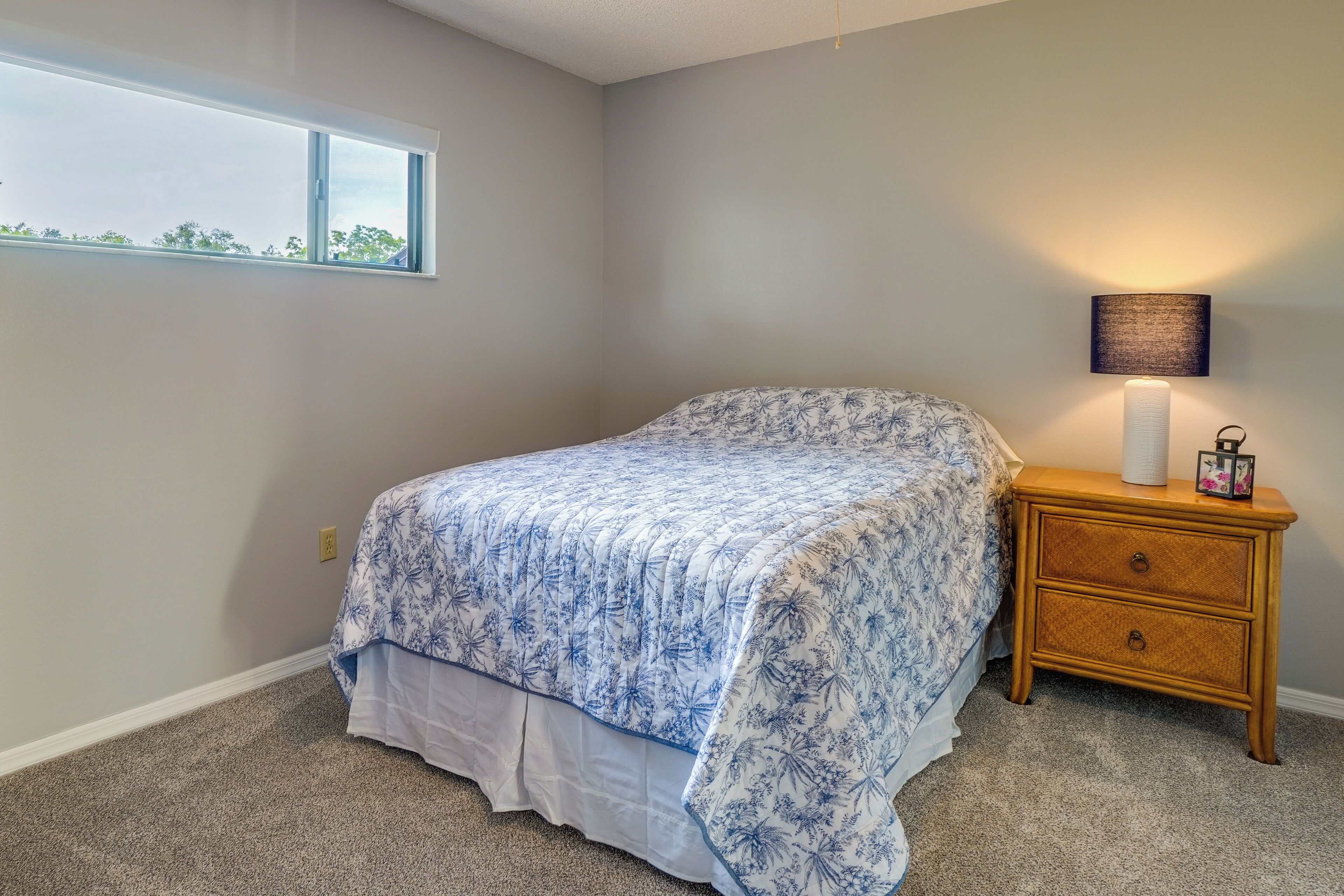 A bedroom with a bed, a nightstand, a lamp, and a window.
