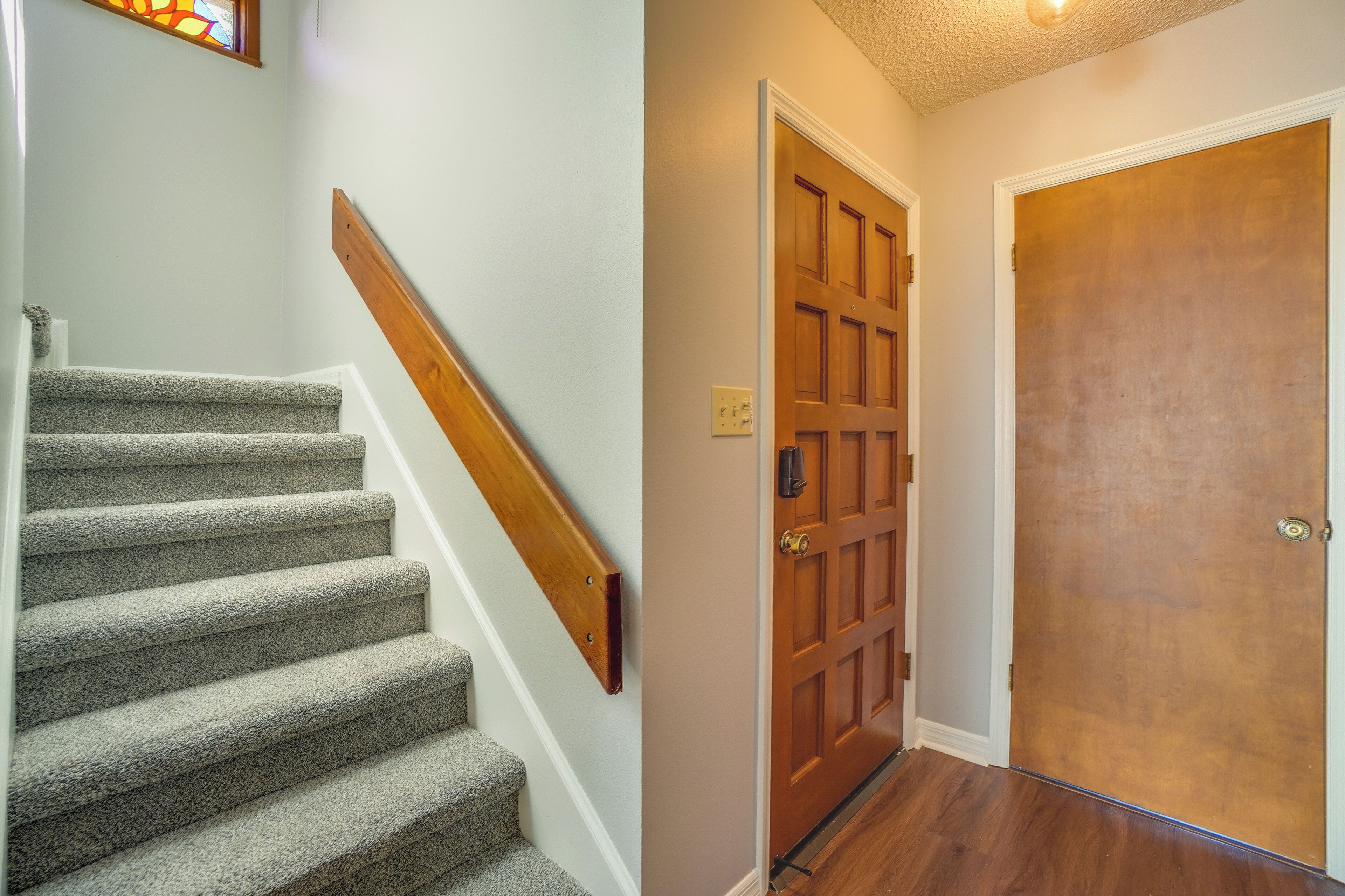 Eine Treppe mit Teppichstufen und einem Holzgeländer, eine Holztür mit Felderung sowie ein Holzboden.