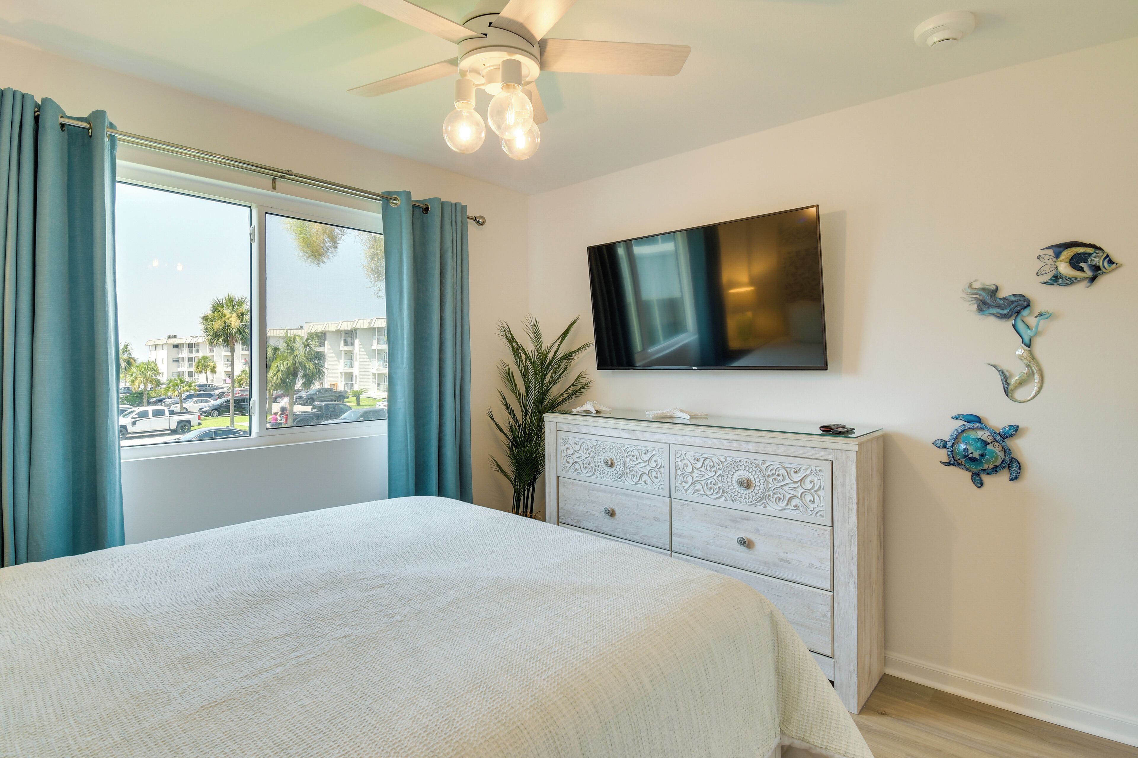 A bedroom with a bed, a dresser, a TV, and a window with curtains.