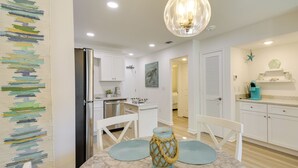 A modern kitchen with white cabinets, a stainless steel refrigerator, and a dining area with a marble table and blue placemats. - Walk to Beach! Gulf Shores Escape w/ Indoor Pool (Gulf Shores)
