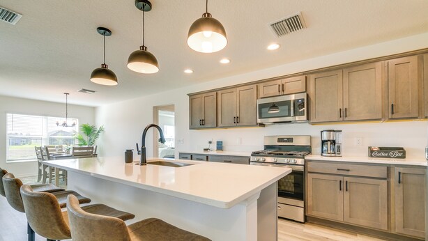 A modern kitchen with a central island, bar stools, stainless steel appliances, and wooden cabinets. - Home w/ Lanai + Community Perks in The Villages! (Okahumpka)