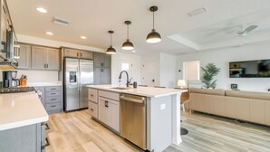A modern kitchen with stainless steel appliances, a central island, pendant lighting, and a large window. - Home w/ Lanai + Community Perks in The Villages! (Okahumpka)
