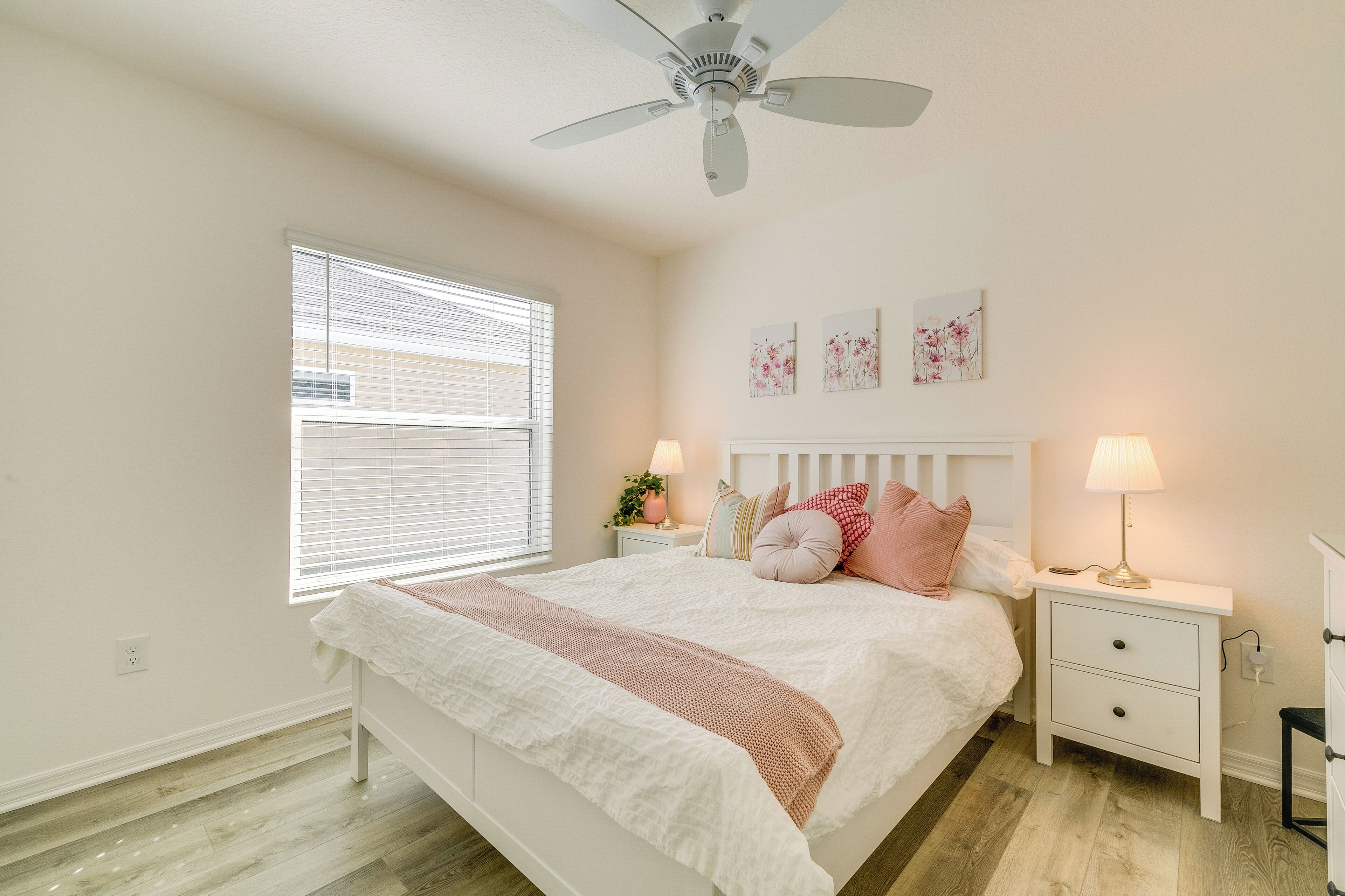 A bedroom with a bed, nightstands, a ceiling fan, and artwork on the wall.