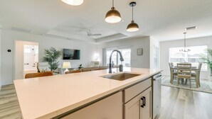 A modern kitchen with a large island, pendant lights, and a dining area with a table and chairs. - Home w/ Lanai + Community Perks in The Villages! (Okahumpka)