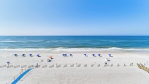 A beach with white sand, a blue sky, and the ocean. There are blue umbrellas and a wooden walkway. - Beachfront Condo in Gulf Shores w/ Pool Access! (Gulf Shores)