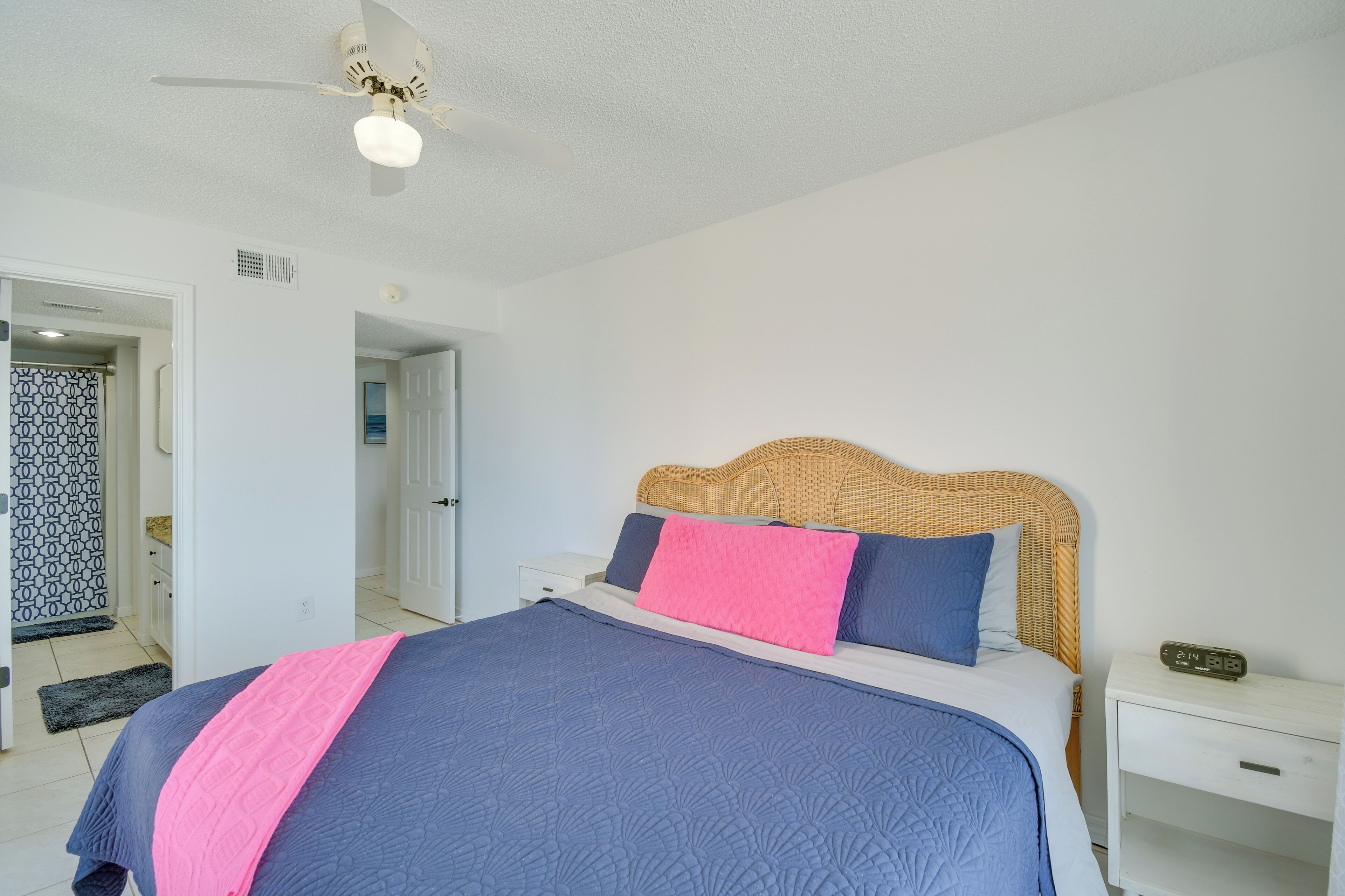 A bedroom with a bed, a nightstand, a ceiling fan, and a door leading to another room.