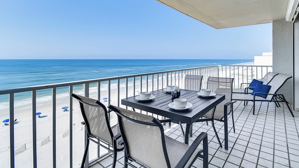 A balcony with a table set for two, overlooking a beach with umbrellas and a clear view of the ocean. - Beachfront Condo in Gulf Shores w/ Pool Access! (Gulf Shores)