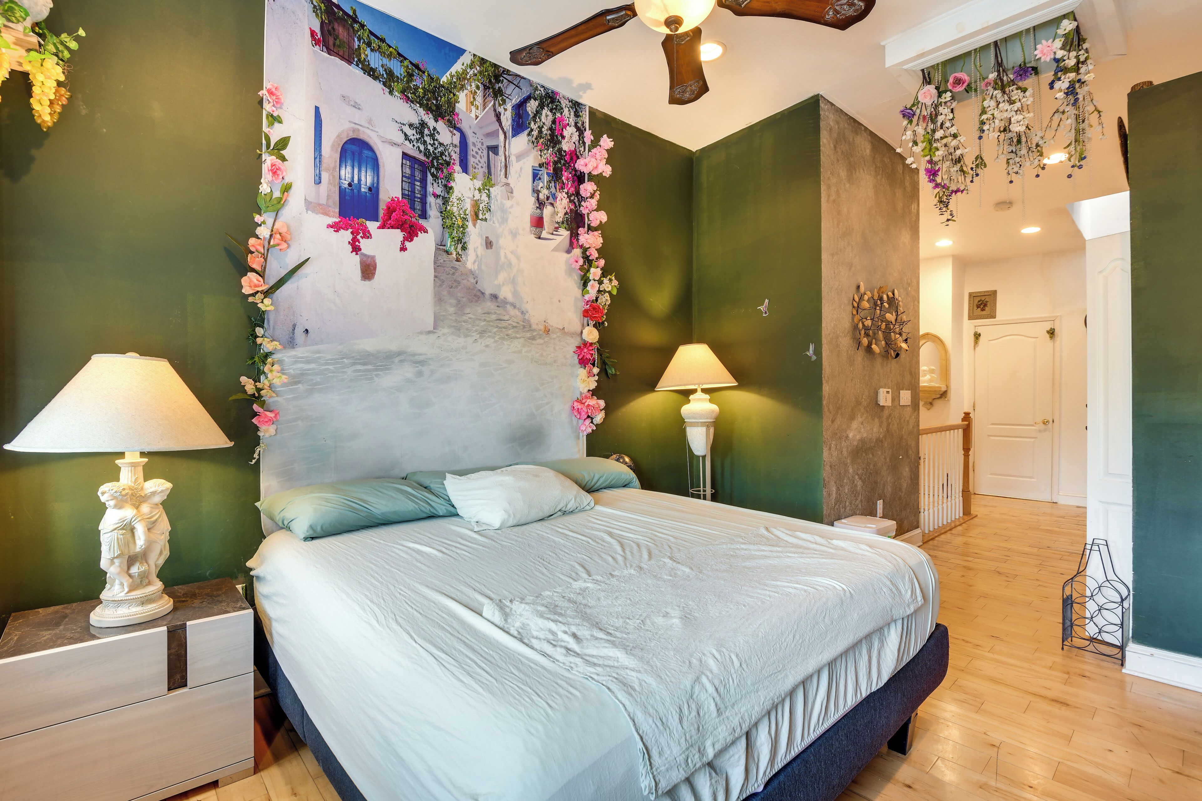 Une chambre à coucher comprenant un lit, deux tables de chevet avec des lampes, une fresque murale et un ventilateur de plafond.