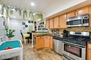 A kitchen with wooden cabinets, a stainless steel stove, a microwave, and a pool table. - Quirky Baltimore Townhome ~ 2 Mi to Inner Harbor (Baltimore)