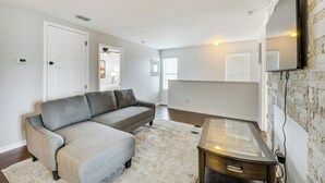 Ein Wohnzimmer mit grauem Ecksofa, einem Couchtisch mit Glasplatte und einer Wand mit Steinoptik.