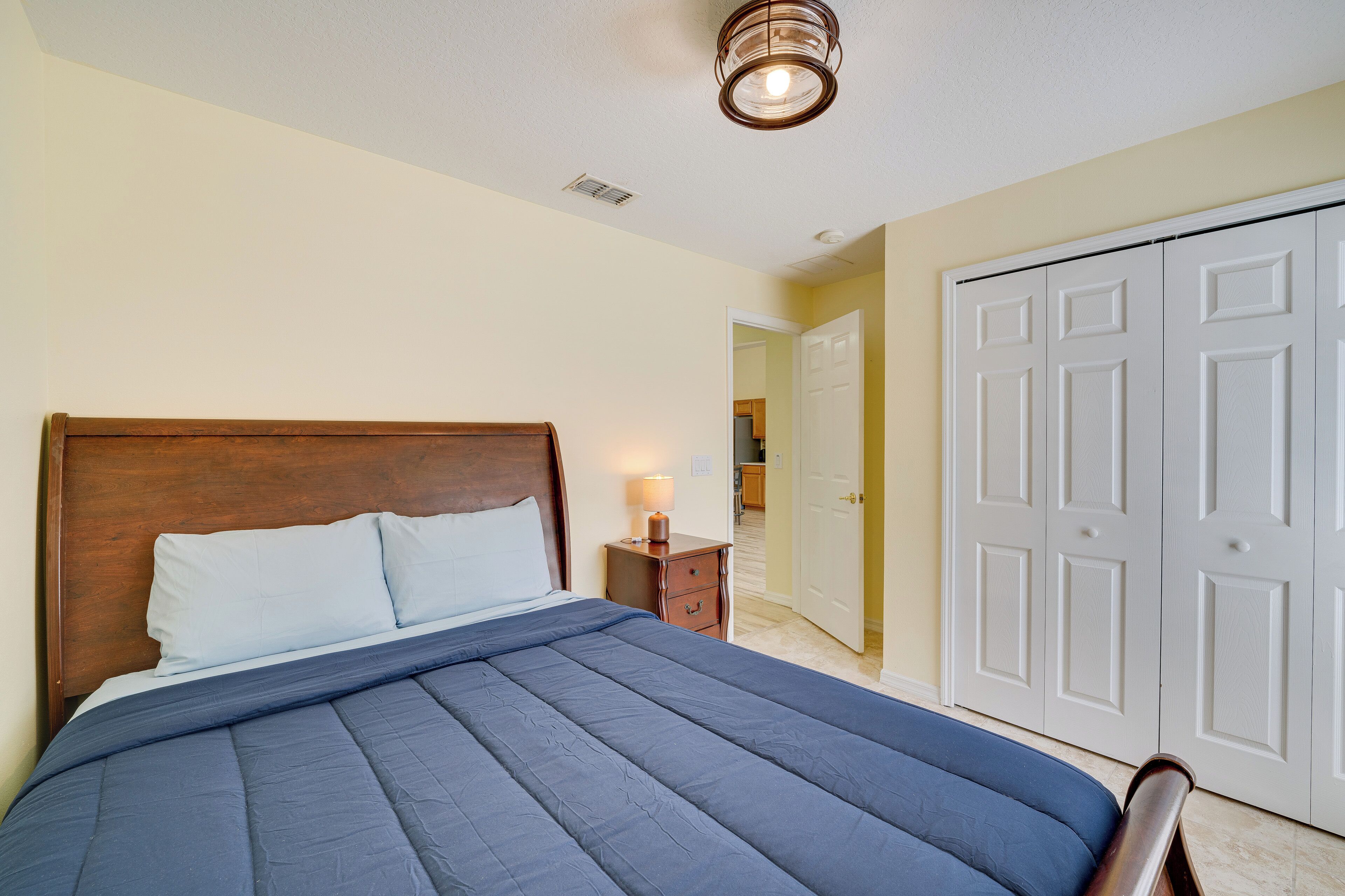 A bedroom with a large bed, a nightstand, a lamp, and a wardrobe.