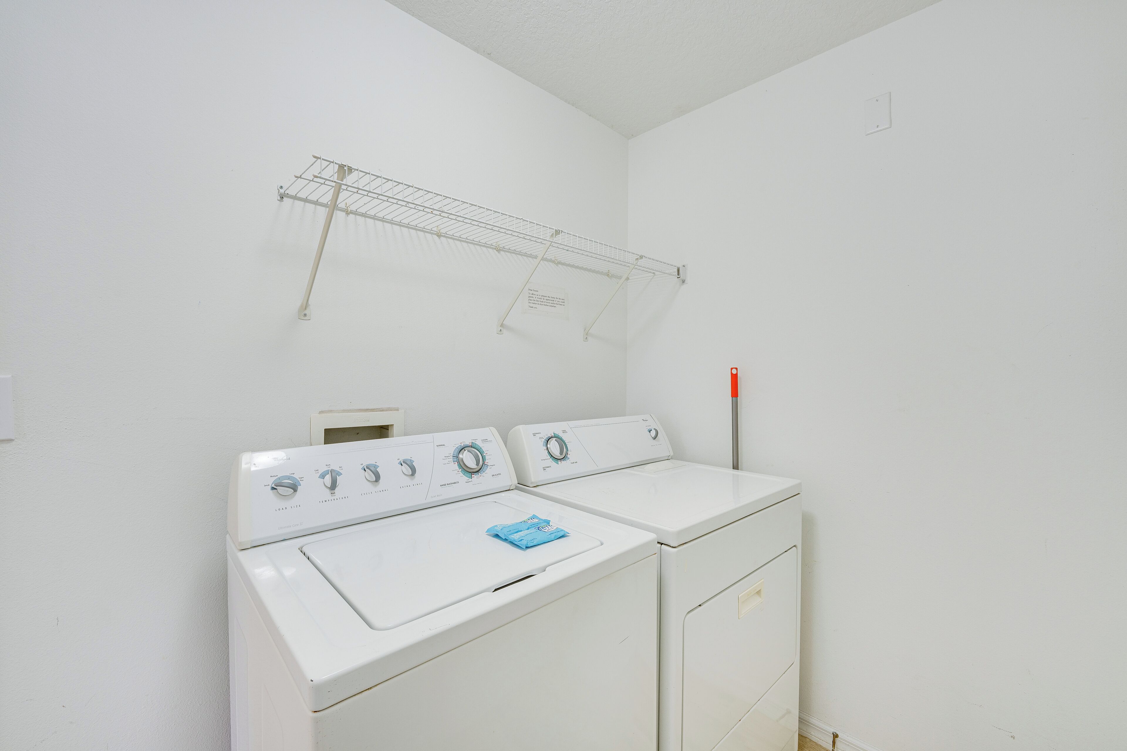 A laundry area with two white washers and dryers, a metal drying rack, and a wall-mounted thermostat.