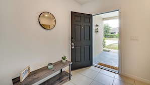 A clean, modern entryway with a dark door, a small bench with a plant, a round mirror, and a welcome mat.