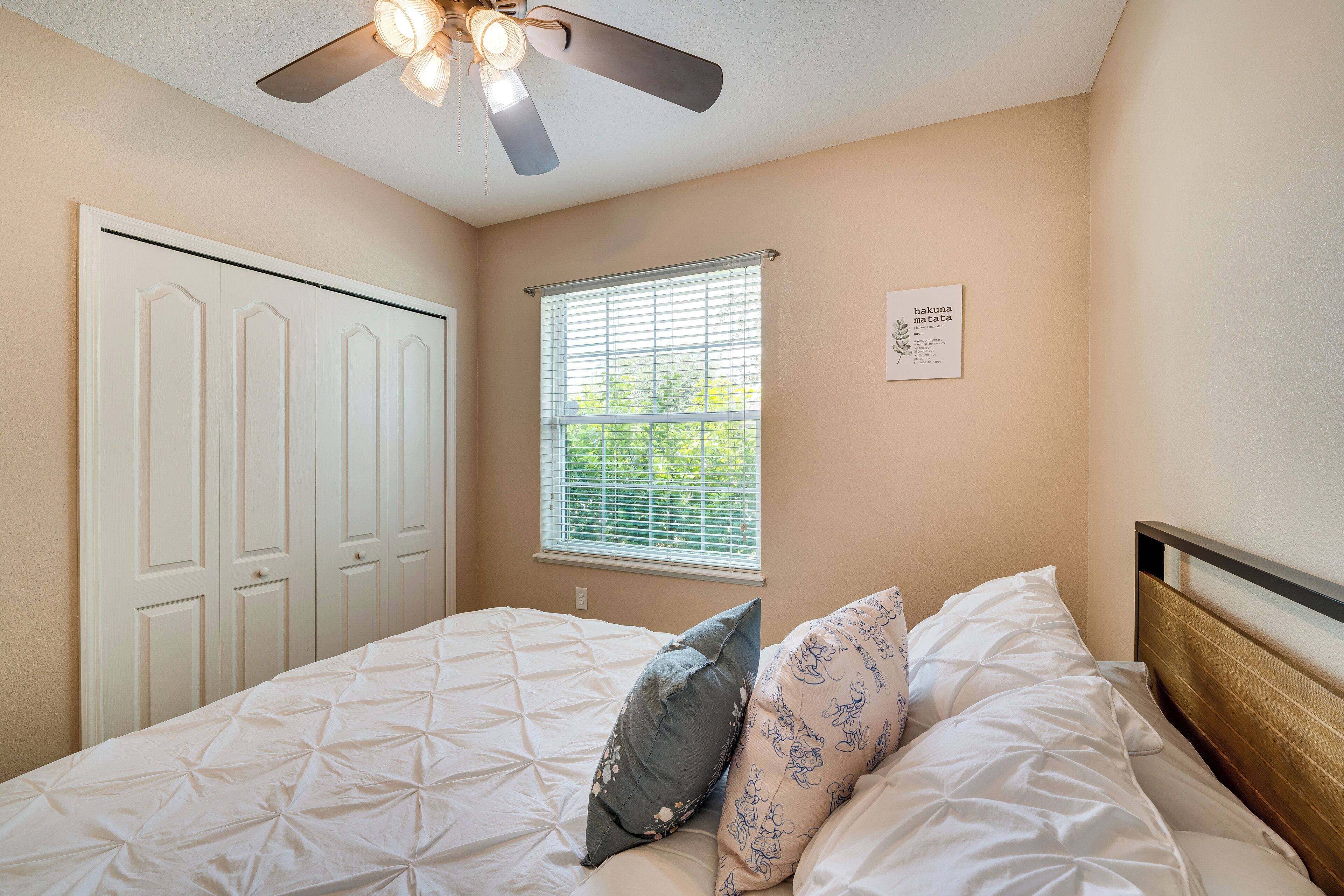 A bedroom with a bed, a ceiling fan, a window with blinds, and a door.