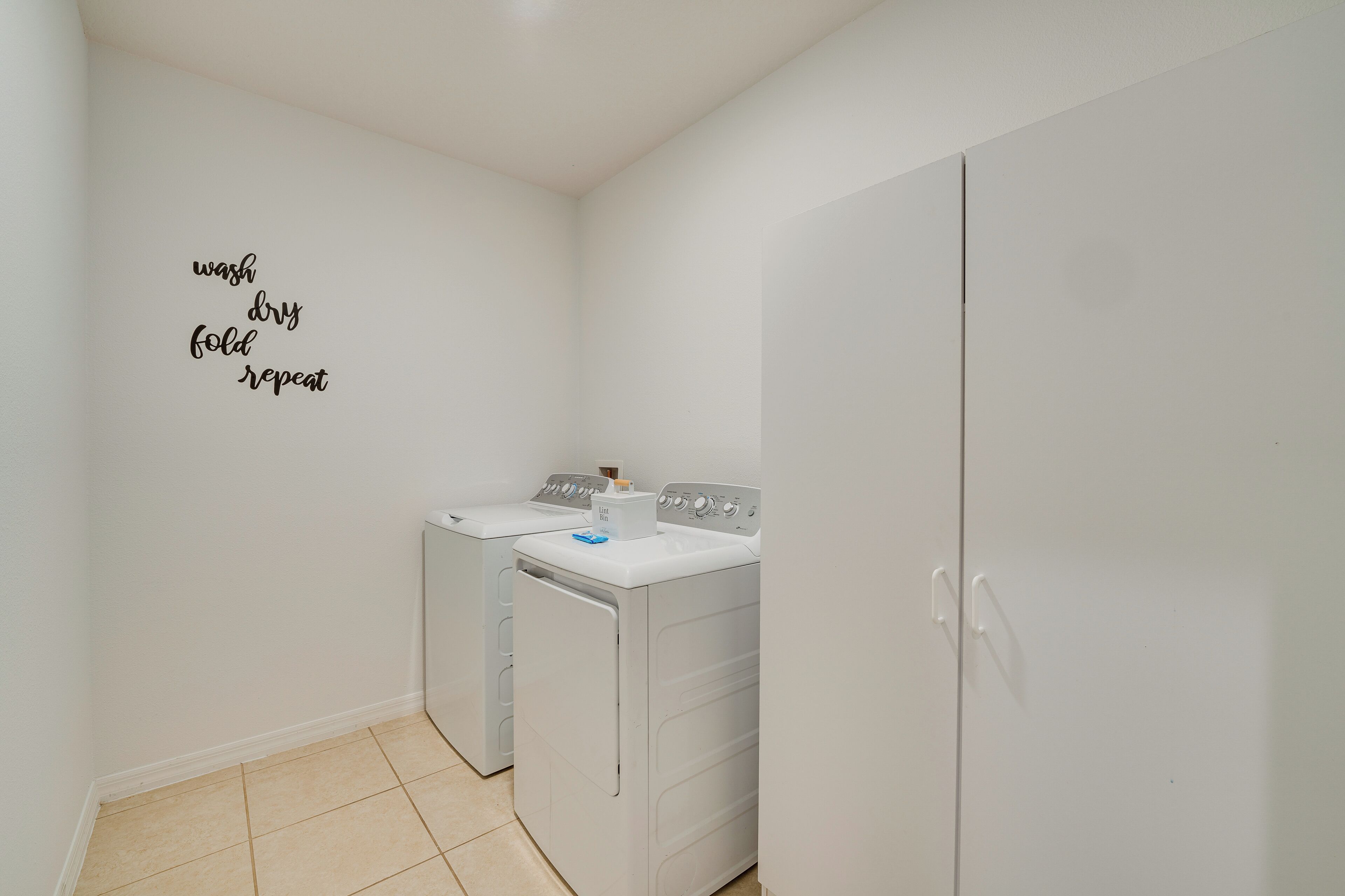 A laundry room with two washing machines and a dryer, a white wall with a laundry instruction sign, and a white door.