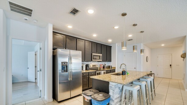 A modern kitchen with stainless steel appliances, a granite countertop, and bar stools.