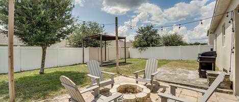 Une terrasse extérieure avec des fauteuils Adirondack, un foyer en pierre et un barbecue.