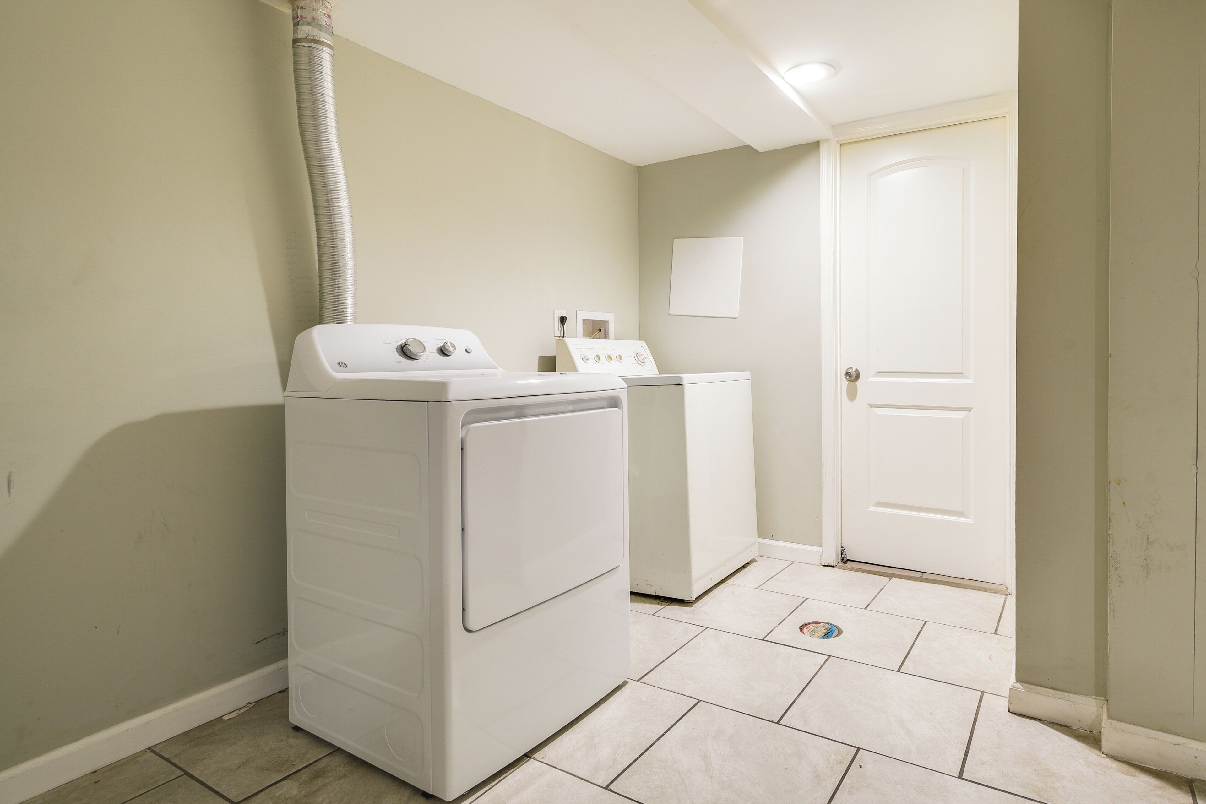 A laundry room with two white washing machines, a dryer, and a vent pipe.