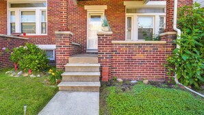 A brick house with a front porch, steps leading to the door, and a small garden area with grass and plants. - Baltimore Vacation Rental - Near JHU & Art Museum! (Baltimore)