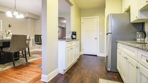 A kitchen with white cabinets, a stainless steel refrigerator, a coffee maker, and a dining area with a table and chairs. - Baltimore Vacation Rental - Near JHU & Art Museum! (Baltimore)