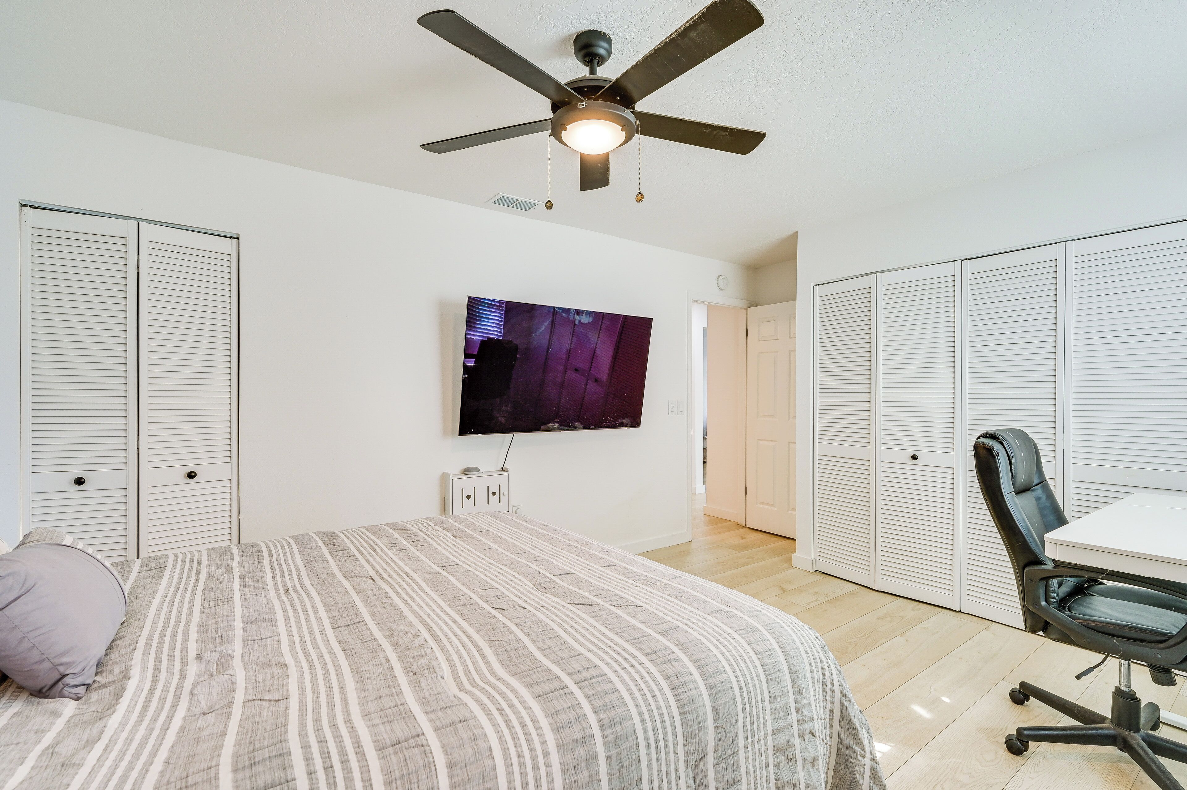 Une chambre à coucher comprenant un lit, un ventilateur de plafond, une télévision, un bureau et des armoires de rangement.