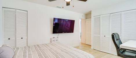Une chambre à coucher comprenant un lit, un ventilateur de plafond, une télévision, un bureau et des armoires de rangement.