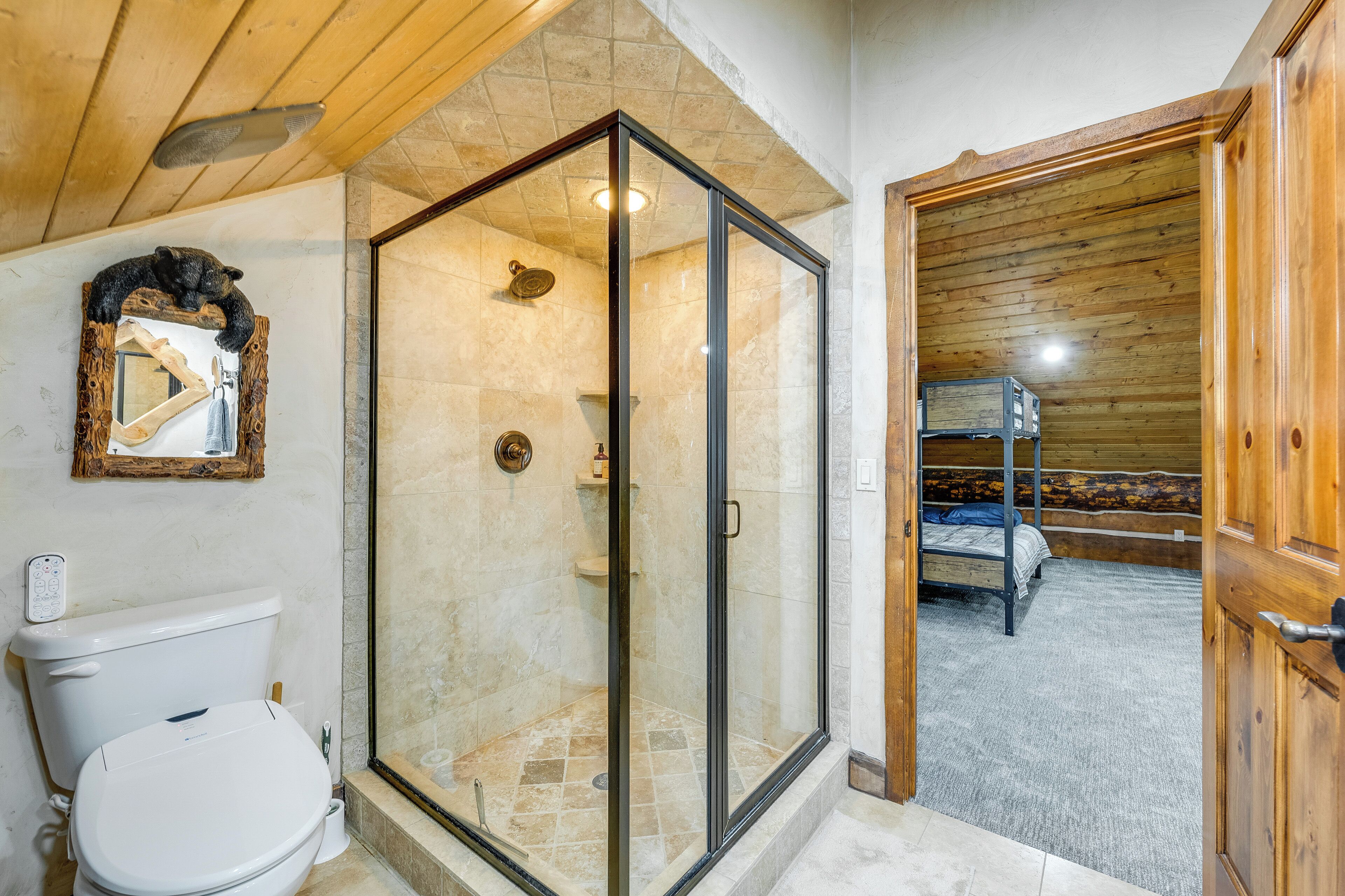 Un baño con ducha envuelta en vidrio, inodoro y techo de madera.
