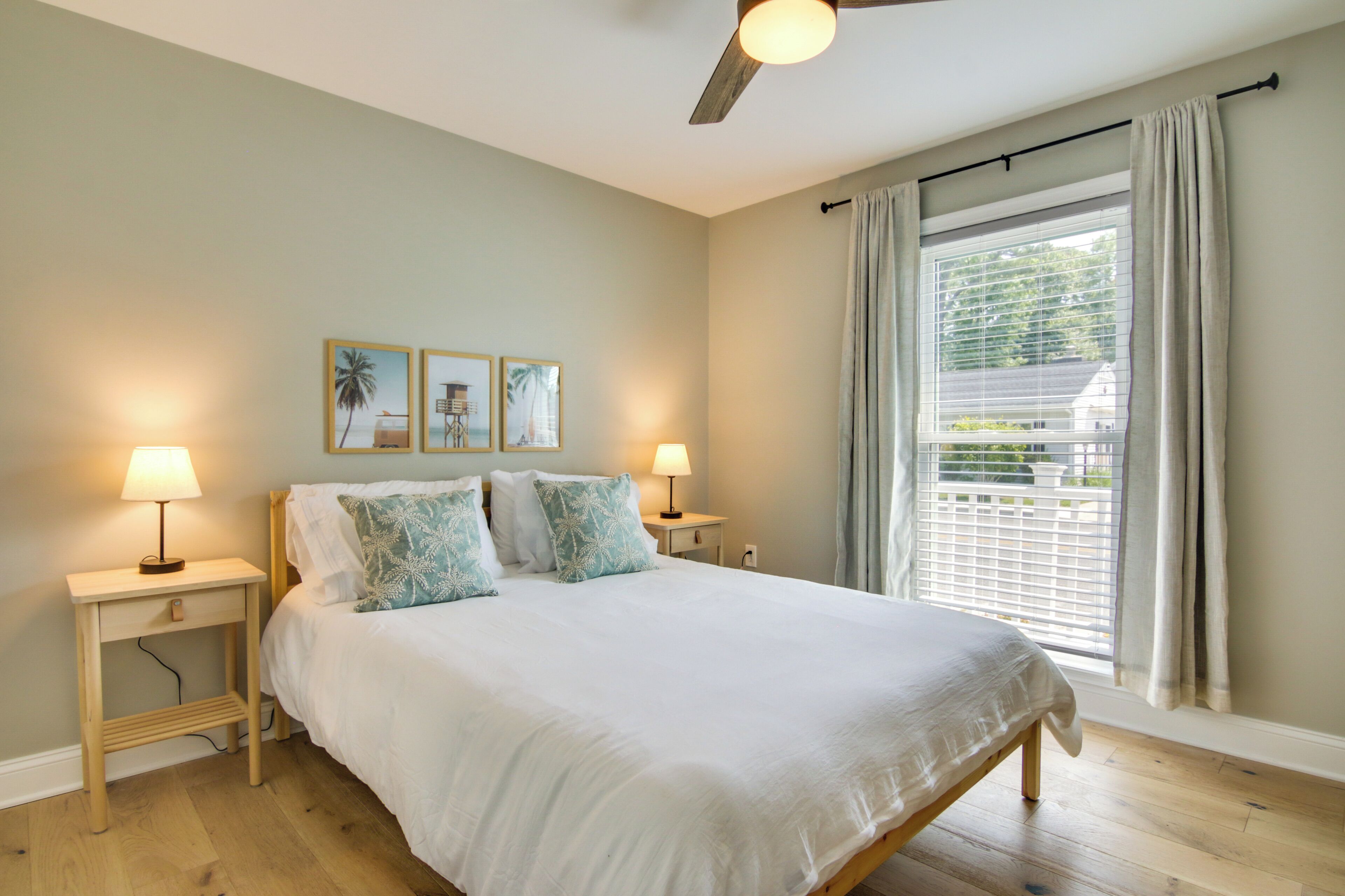 A bedroom with a bed, two bedside tables, a ceiling fan, and a window with curtains.