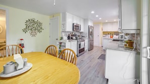 A modern kitchen with white cabinets, stainless steel appliances, and a dining area with a wooden table and chairs.